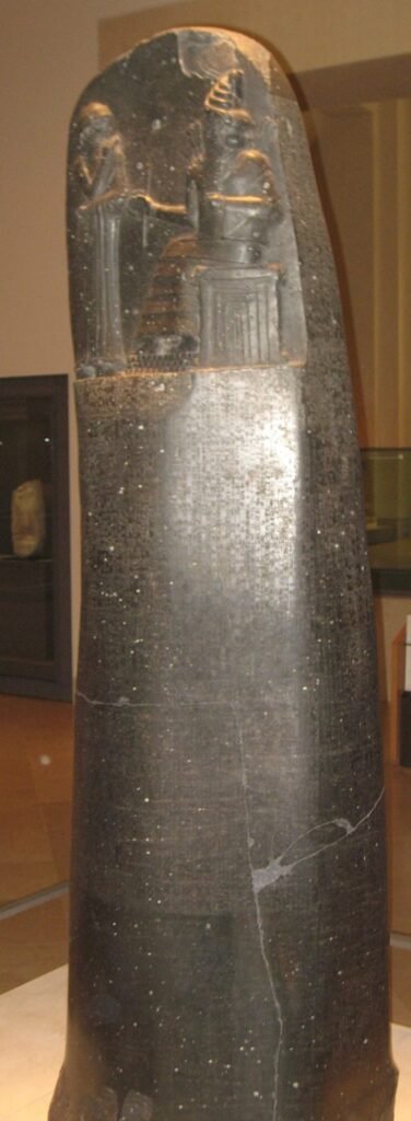 Tall black stone pillar carved with rows of cuneiform text, on display in a museum